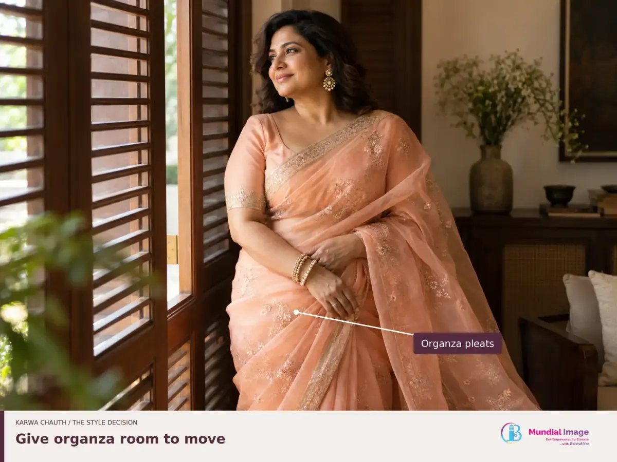 Woman in a peach organza saree beside a window, with the volume of its pleats highlighted.